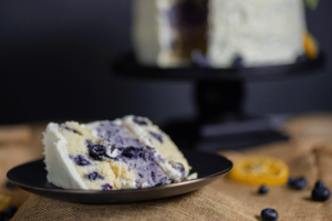 slice of Blueberry Lemon cake with full cake in background studio image Dave Gevry Photography 2025